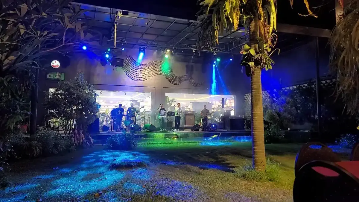 Taman Sasaku Bar & Resto pada malam hari dengan lampu biru dan panggung